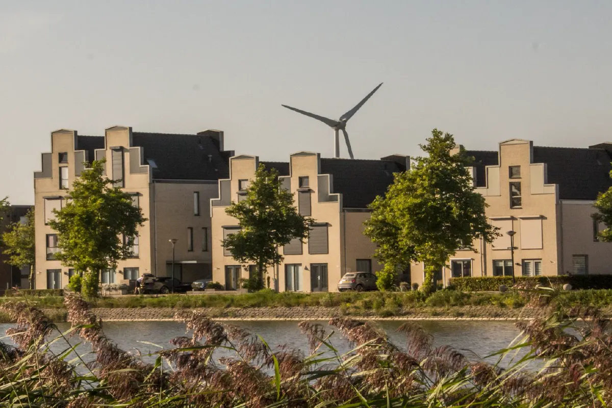 Stad van de Zon met duurzame woningen langs water en een windmolen op de achtergrond.